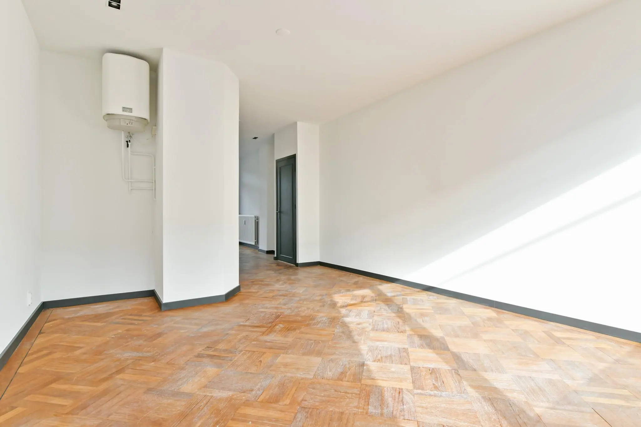 Lichte, lege kamer aan de Cornelis Dopperkade met houten visgraatvloer, witte muren en een boiler aan de muur.